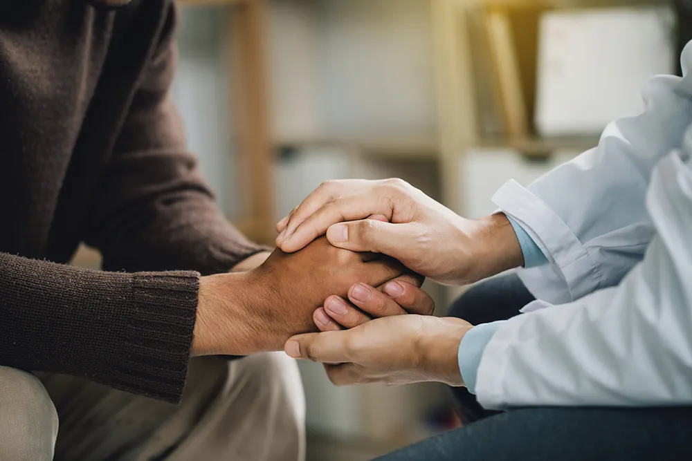 Jens Mehrens behandelt einen Patienten in einem vertraulichen Verhältnis zur Seelsorge durch empathische Berührung der Patientenhände in seiner psychotherapeutischen Praxis in Swisttal bei Euskirchen.