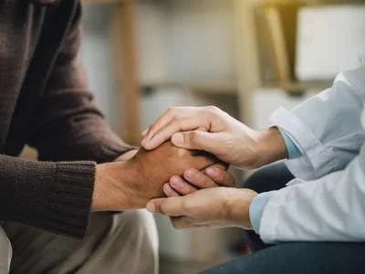 Jens Mehrens behandelt einen Patienten in einem vertraulichen Verhältnis zur Seelsorge durch empathische Berührung der Patientenhände in seiner psychotherapeutischen Praxis in Swisttal bei Euskirchen.